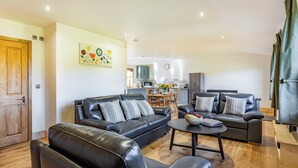 A modern living room with leather sofas, a coffee table, and a kitchen in the background.