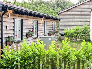 A wooden house with a picket fence, a wooden utility box, and potted plants on the windowsills.