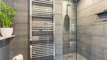 A modern bathroom with a glass shower enclosure, a towel rack, and a potted plant.