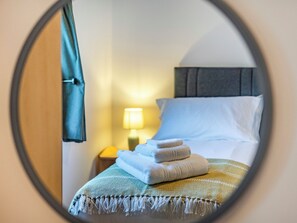 A hotel room with a bed, a nightstand, a lamp, and a view through a circular mirror.