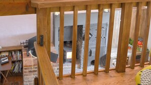 A wooden balcony railing overlooking a fireplace area with a brick wall and a bookshelf. - The Old Back Kitchen at Bonfield Ghyll Farm (Helmsley)