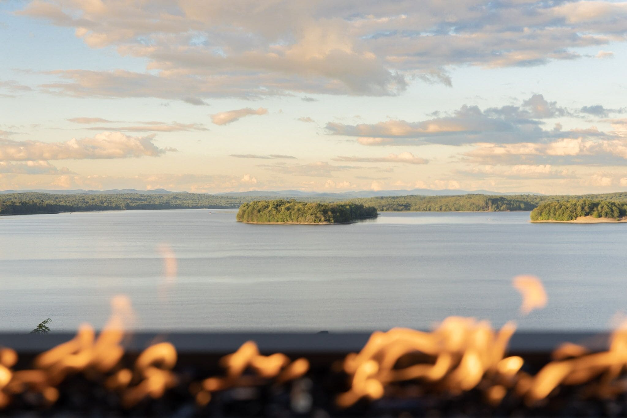 A calm lake with two small islands, surrounded by forested hills.