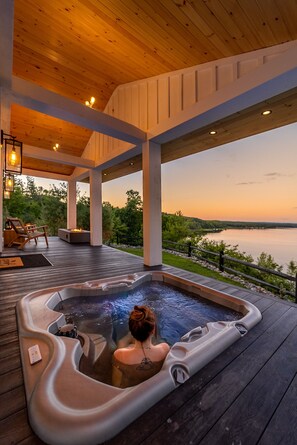 A hot tub on a wooden deck with a view of a lake at sunset. - ADIRONDACK LUXURY MODERN LAKEFRONT VILLA WITH HOTUB!! BRAND NEW BUILD!! (Remsen)