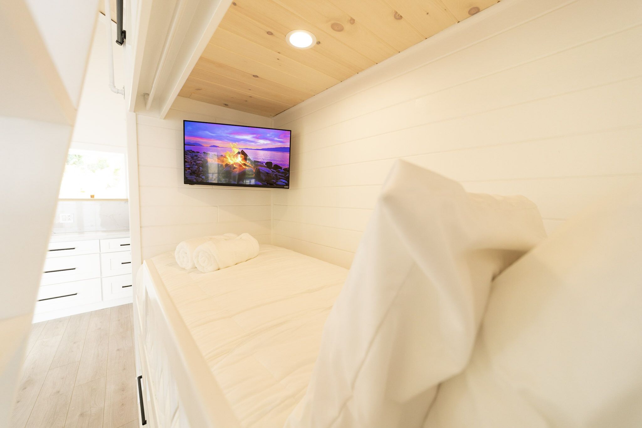 A bedroom with a bed, a TV mounted on the wall, and a wooden ceiling.