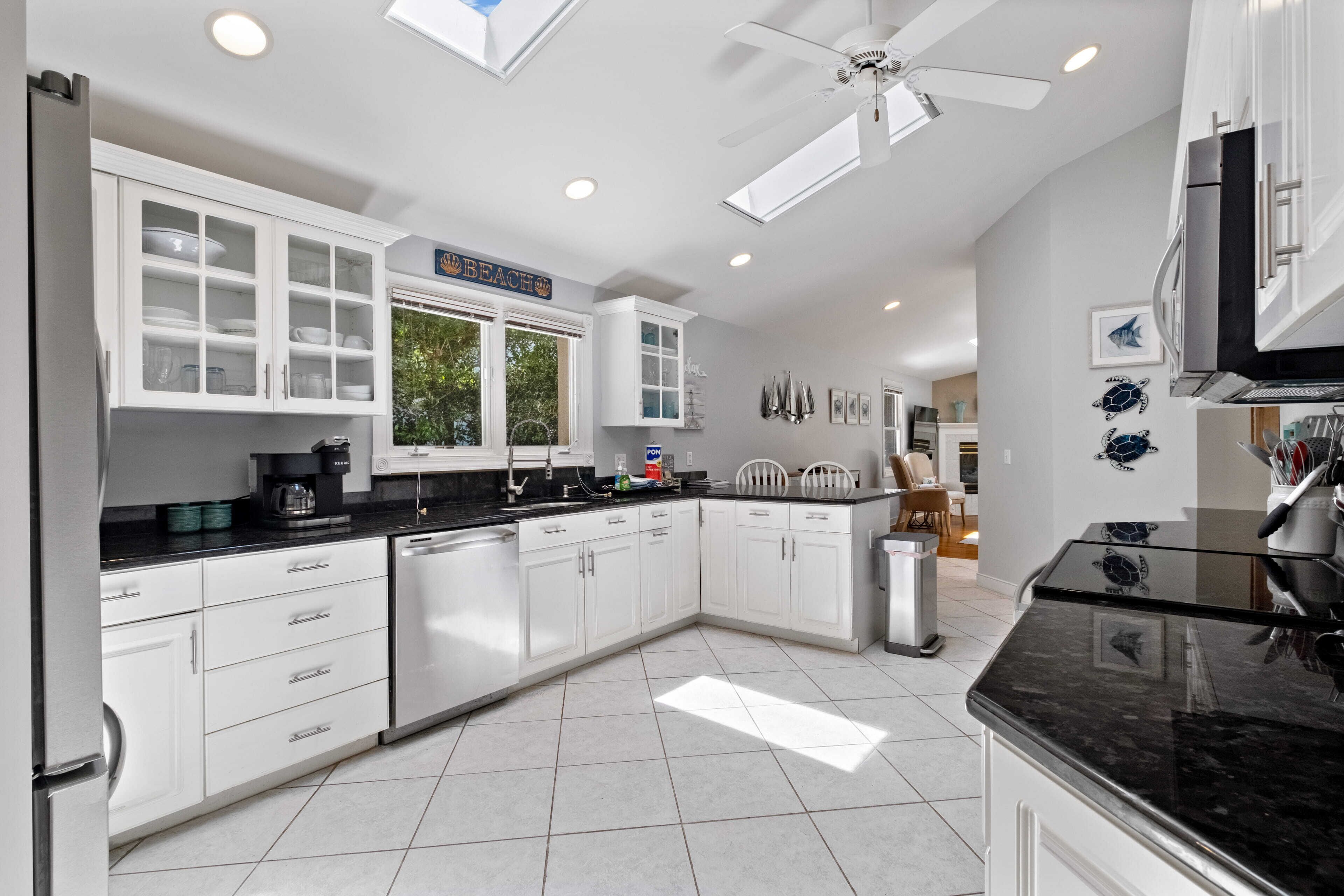 A modern kitchen with white cabinets, a black countertop, and a ceiling fan.