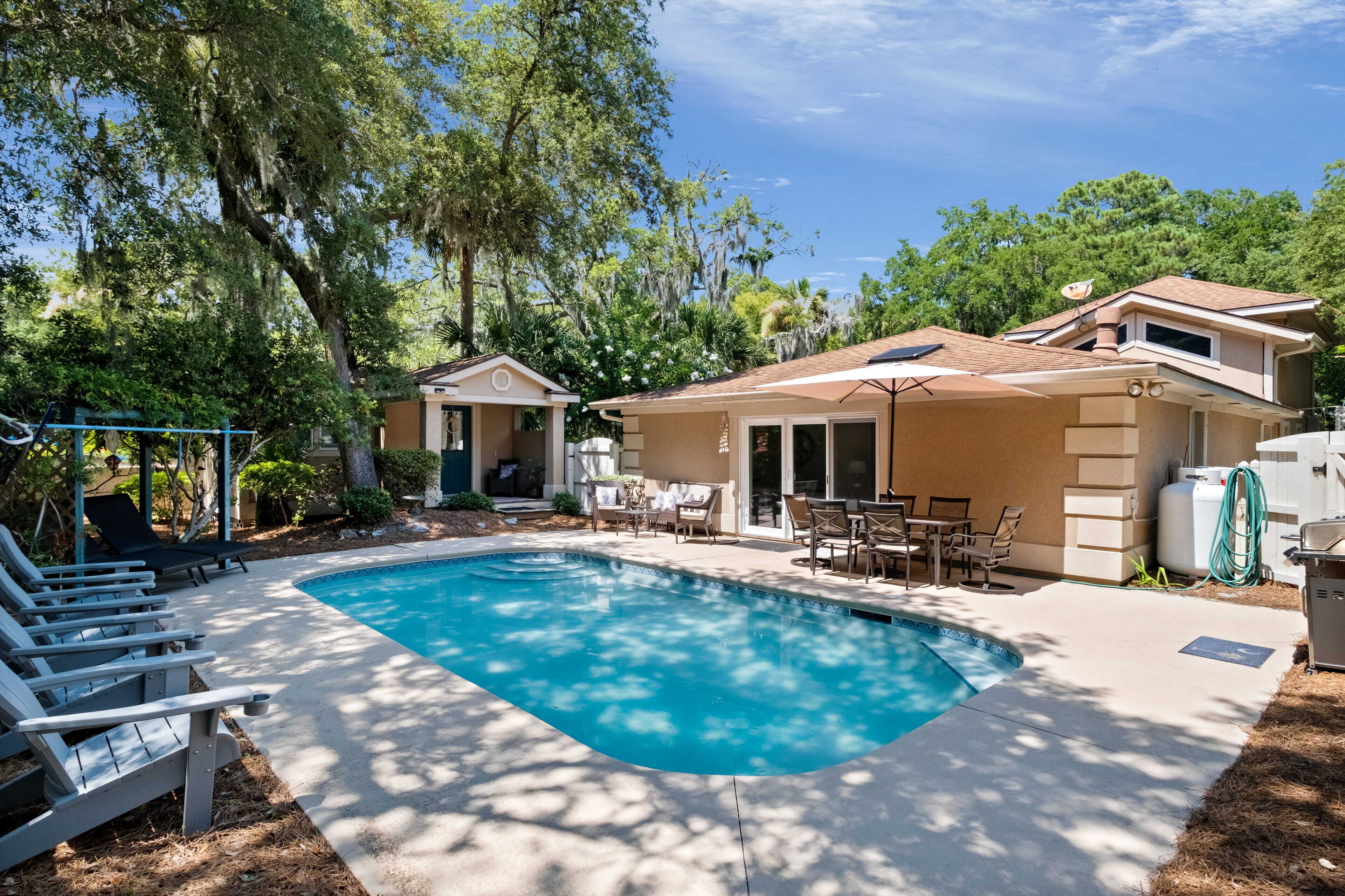 A backyard with a swimming pool, lounge chairs, and a patio area with outdoor furniture.