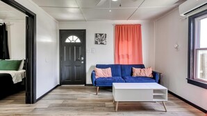 A modern living room with a blue sofa, white coffee table, and a black door with a window. - The Bluebird: Modern 1 Bed, Large Peaceful Yard (Joplin)