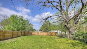 A fenced backyard with a grassy lawn, a wooden fence, and a large tree. - The Bluebird: Modern 1 Bed, Large Peaceful Yard (Joplin)