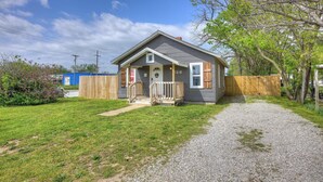A single-story house with a front porch, a gravel driveway, and a wooden fence. - The Bluebird: Modern 1 Bed, Large Peaceful Yard (Joplin)