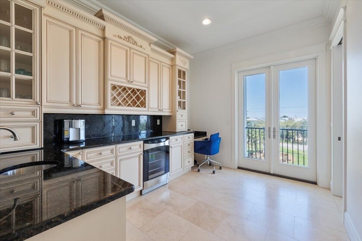 A spacious kitchen with cream cabinetry, a black countertop, and a view of the outdoors through large sliding glass doors.