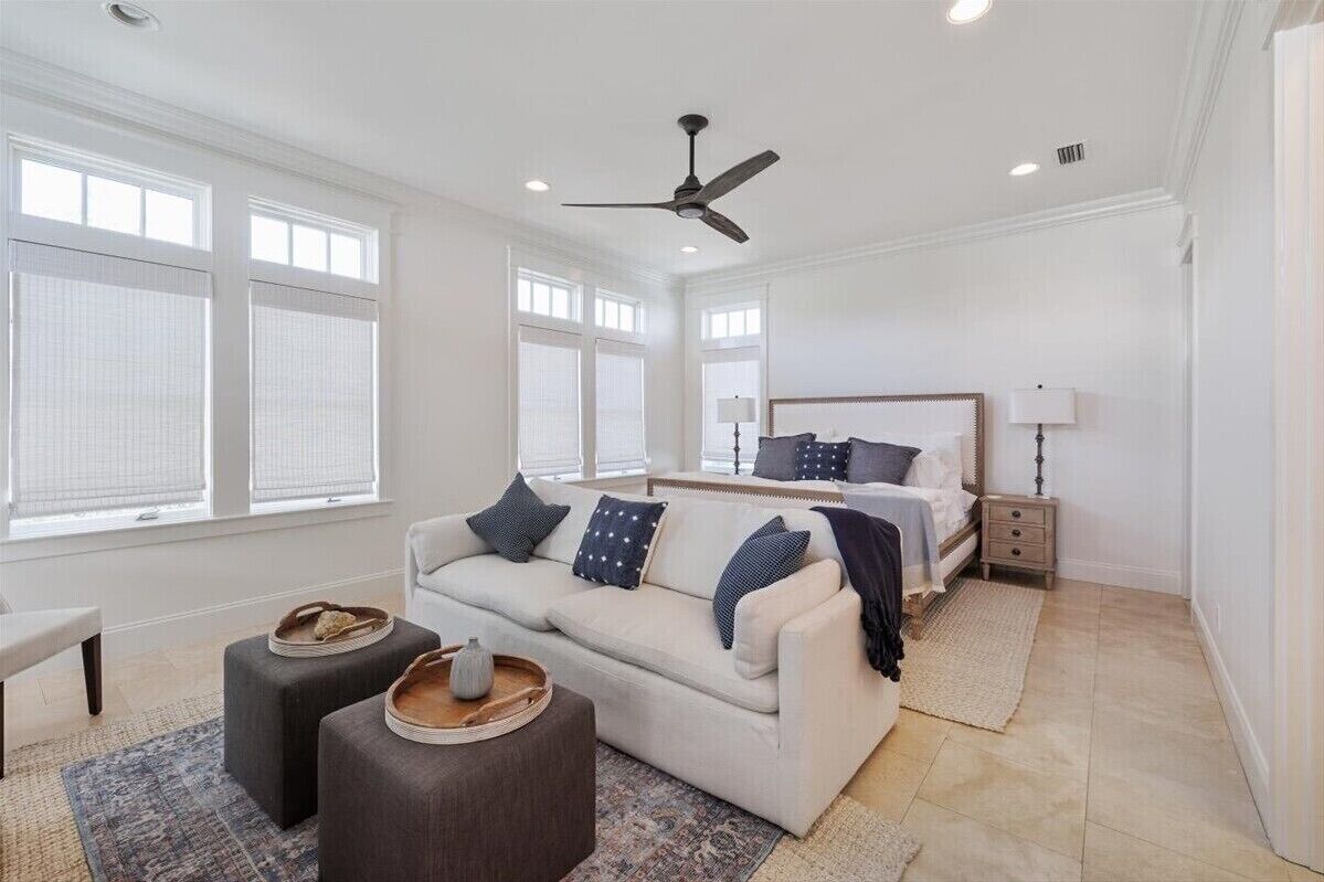 A modern bedroom with a bed, a sofa, a desk, and a ceiling fan.