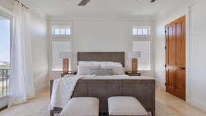 Quarto com uma cama grande, duas mesas de cabeceira, uma porta de madeira e vista pela janela.