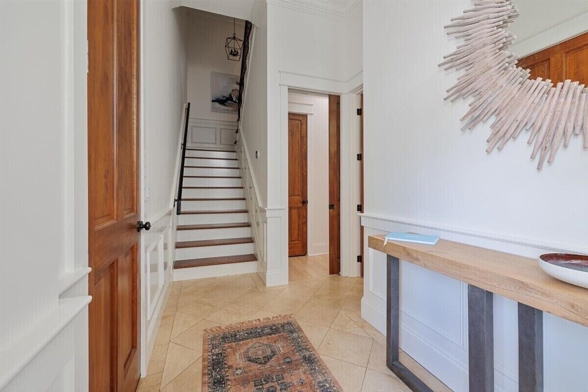 A hallway with a wooden door, a staircase, a patterned rug, and a wall-mounted decorative piece.