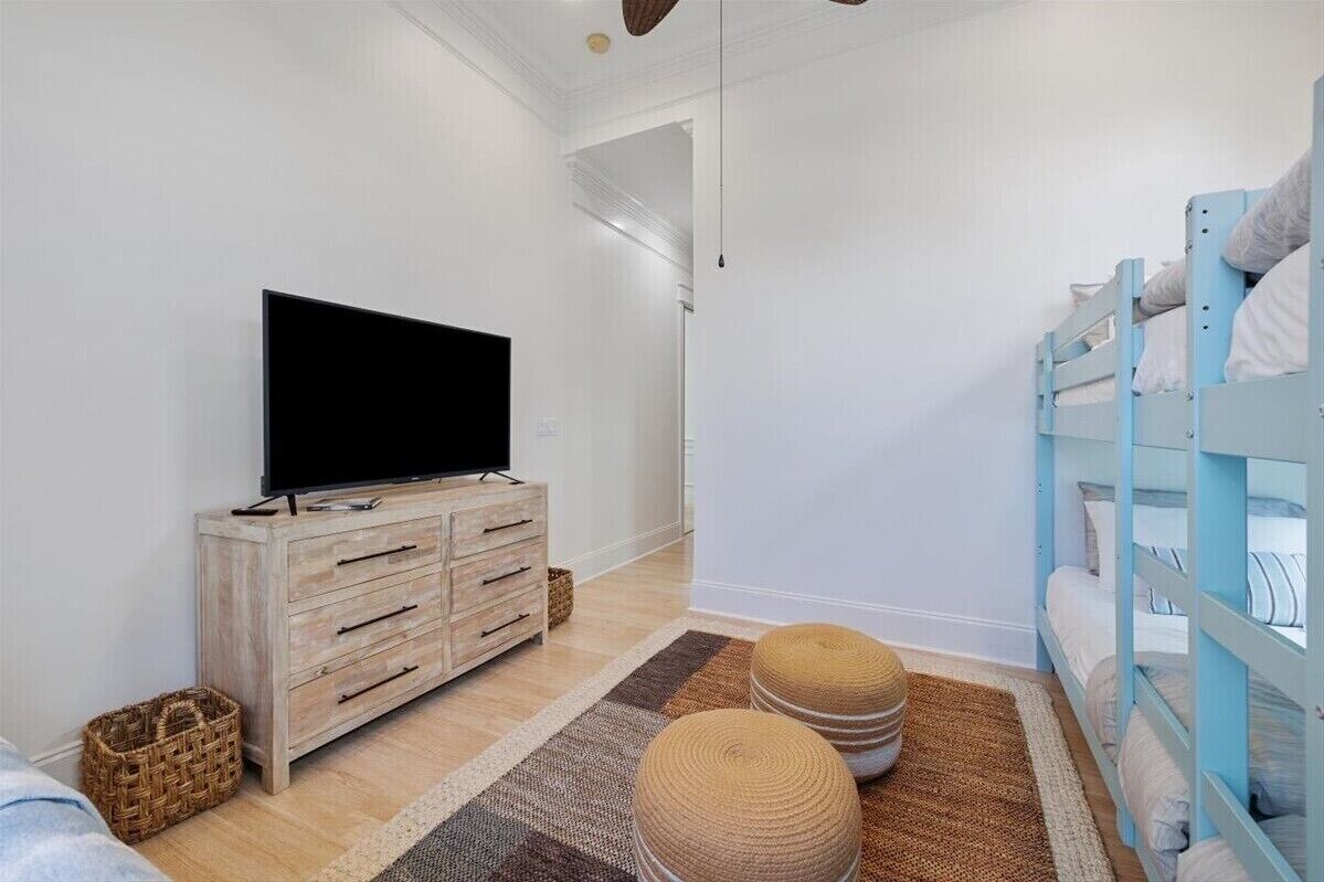 A modern bedroom with a TV on a wooden dresser, a bunk bed, and a woven rug.