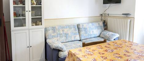 Ett rum med en soffa, ett skåp, en tv och ett bord.
