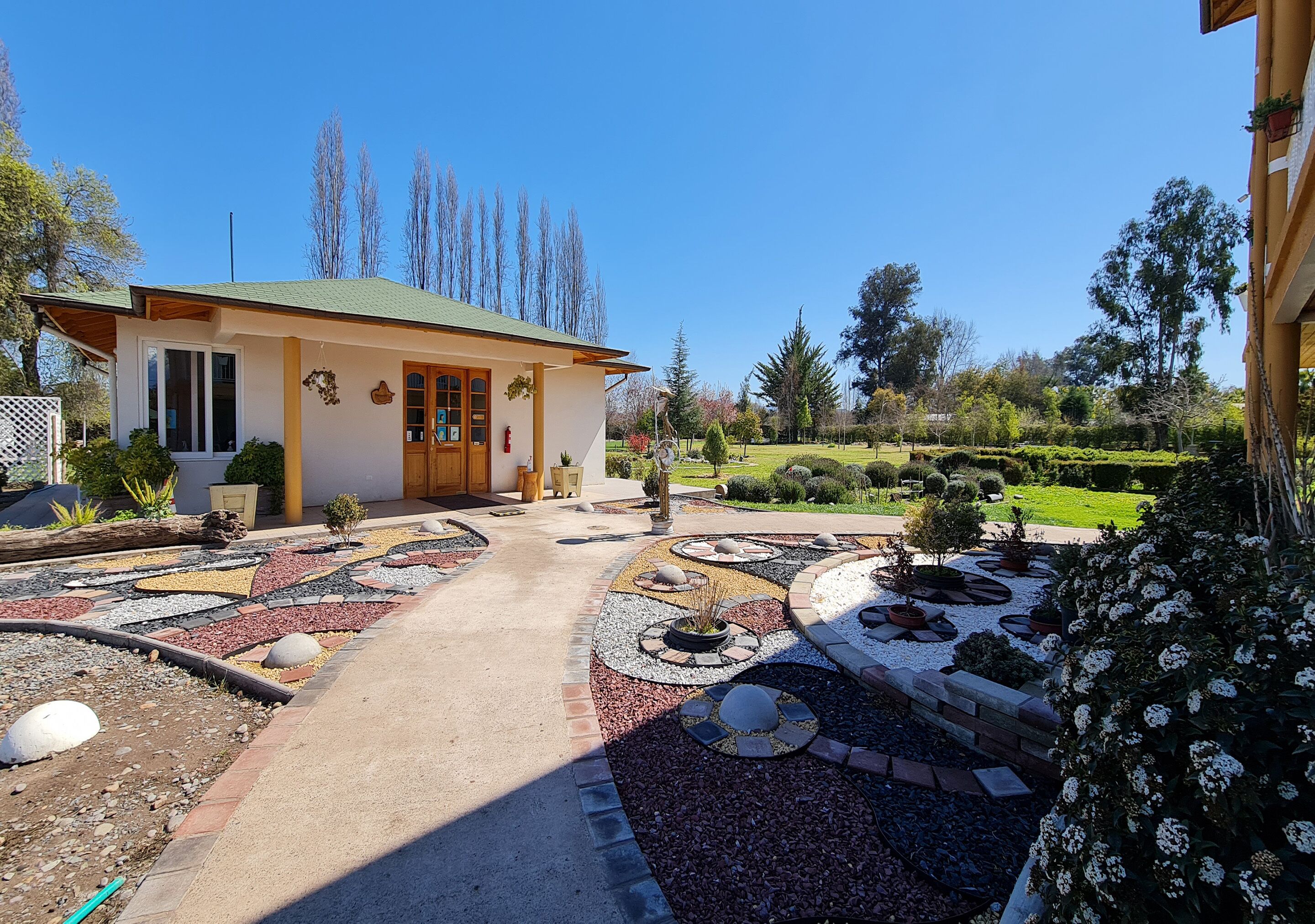 A house with a green roof, a paved driveway, and a garden with various plants and a circular stone design.