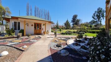 A house with a green roof, a paved driveway, and a garden with various plants and a circular stone design.