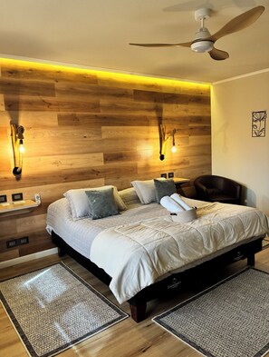 A bedroom with a bed, two wall-mounted light fixtures, a ceiling fan, and a wooden wall panel. - Hotel El Almendro (Buin)