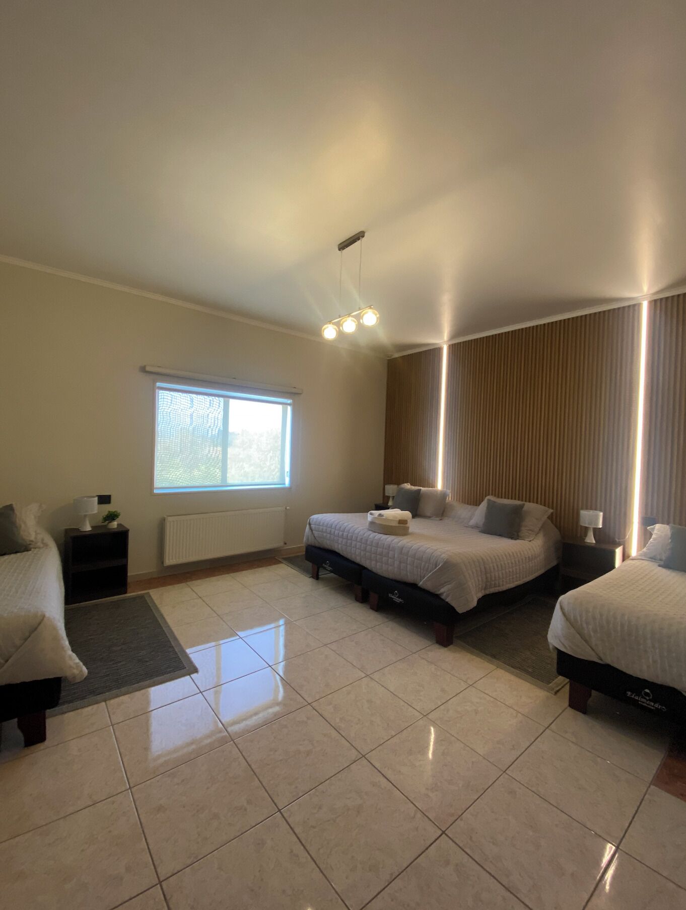 A bedroom with two beds, a window, a radiator, and a ceiling light fixture.