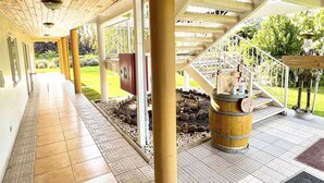 Un pasillo cubierto con techo de madera, suelo de baldosas de piedra y vistas a un jardín.