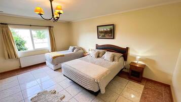 A hotel room with two beds, a chandelier, a painting, and a window with curtains.