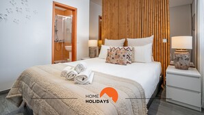 A modern hotel room with a large bed, wooden panel wall, and two bedside tables with lamps. - #094 Maresia Flats by Home Holidays (Albufeira)