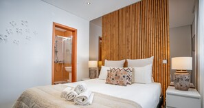 A modern hotel room with a large bed, wooden panel wall, and two bedside tables with lamps.