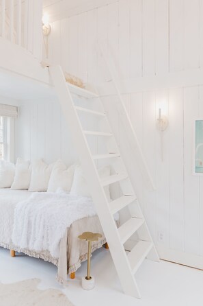 Cozy retreat with a plush bed, ladder to a loft, and a small table for relaxation.