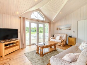 A spacious living room with a large TV, wooden entertainment unit, and a cozy seating area with a sofa and armchair.