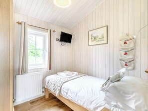 A bedroom with a wooden bed, white bedding, a window with curtains, a mounted TV, and a wall-mounted towel rack.