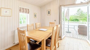 Een eetgedeelte met een houten tafel en stoelen, een radiator en uitzicht door een glazen deur op een terras.