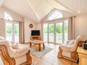 A spacious living room with a wooden ceiling, large windows, a television, and two leather sofas.
