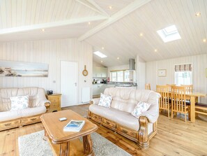 En rummelig stue med to sofaer, et træsofabord og et spiseområde med et bord og stole.