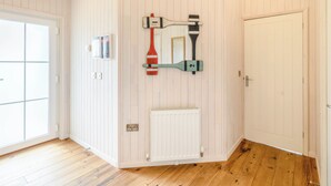 Een kamer met witte paneelwanden, een houten vloer, een radiator, een deur en een wandspiegel met een suppenplank en peddel.