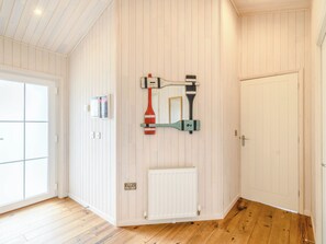 A room with white paneled walls, a wooden floor, a radiator, a door, and a wall-mounted mirror with a paddleboard and paddle.