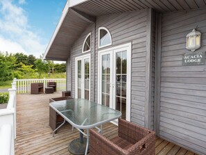 A covered outdoor area with a glass table and wicker chairs, a white railing, and a sign reading "ACACIA LODGE".