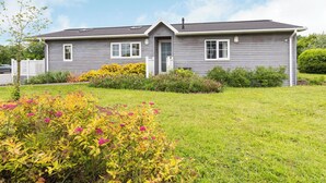 Een huis met twee verdiepingen, een voortuin, een garage en een verzorgde tuin met verschillende bloeiende planten.