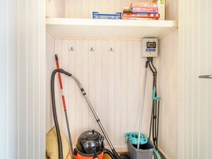 A storage closet with shelves holding various items, including a vacuum cleaner, a mop, and a power strip.