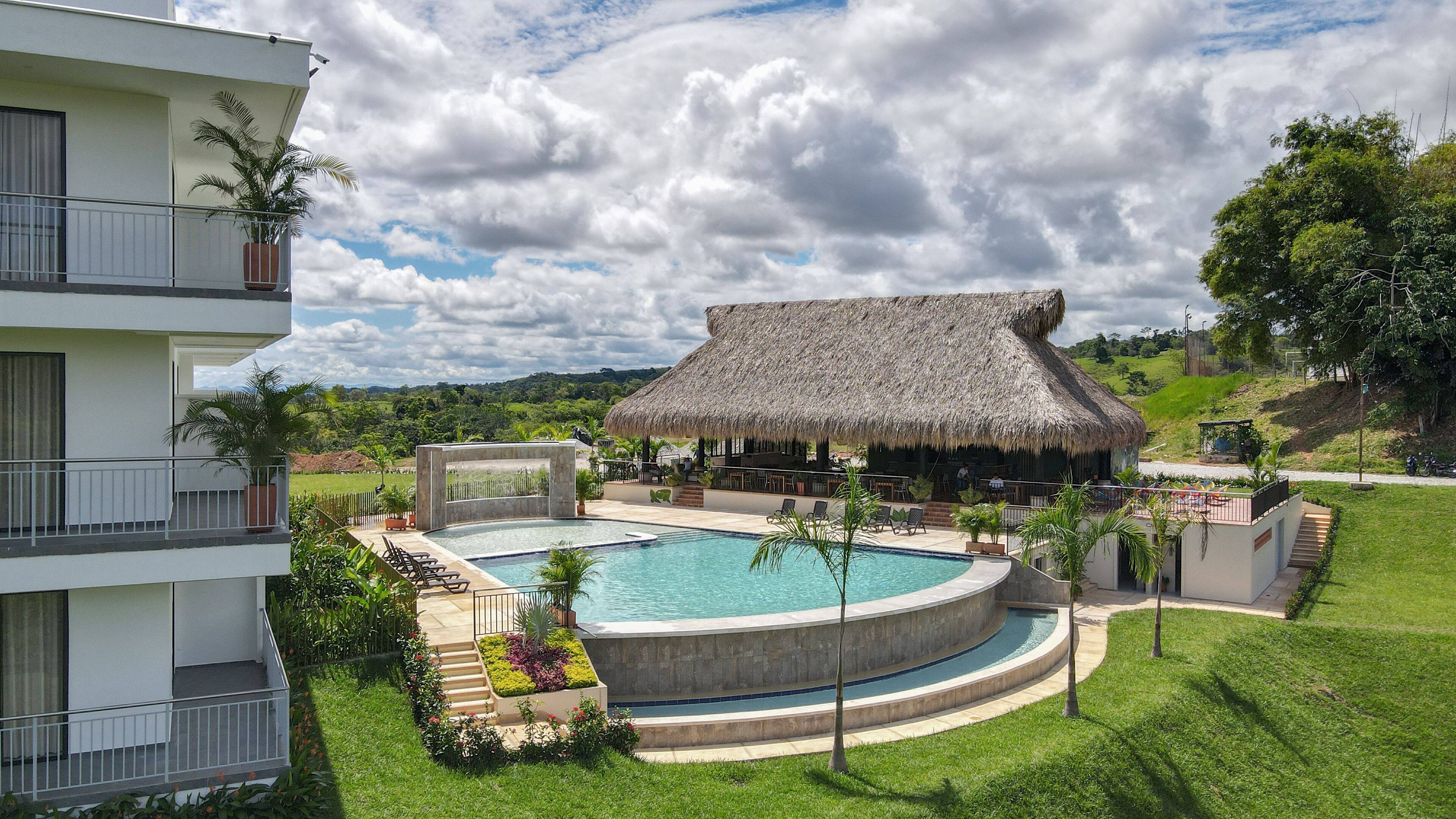 Un complexe hôtelier doté d’une piscine, d’une structure à toit de chaume et d’un paysage verdoyant luxuriant.