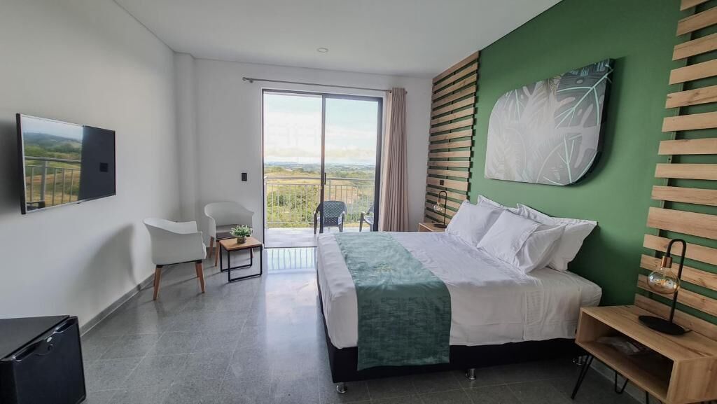 A modern hotel room with a bed, a chair, a desk, a TV, and a view of the outdoors.