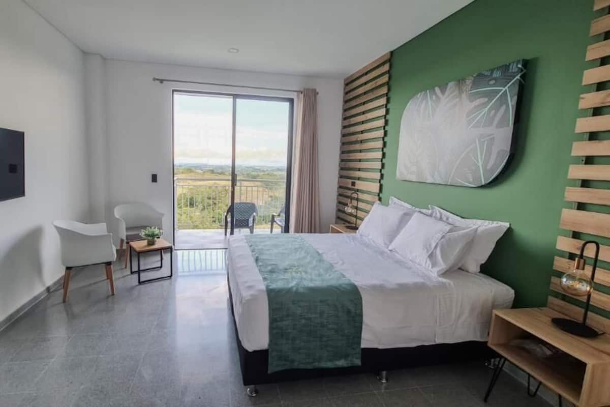 A modern hotel room with a bed, a chair, a desk, a TV, and a view of the outdoors.