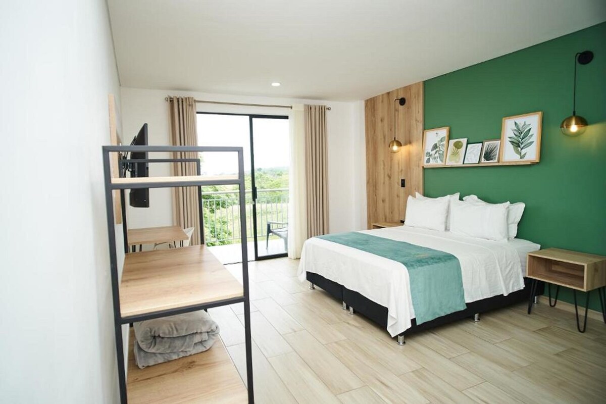 Ein Schlafzimmer mit Etagenbett, einem Bett mit weißer Bettwäsche, einer grünen Wand mit gerahmten Pflanzenmotiven, einem Nachttisch aus Holz und Blick durch eine Glastür.