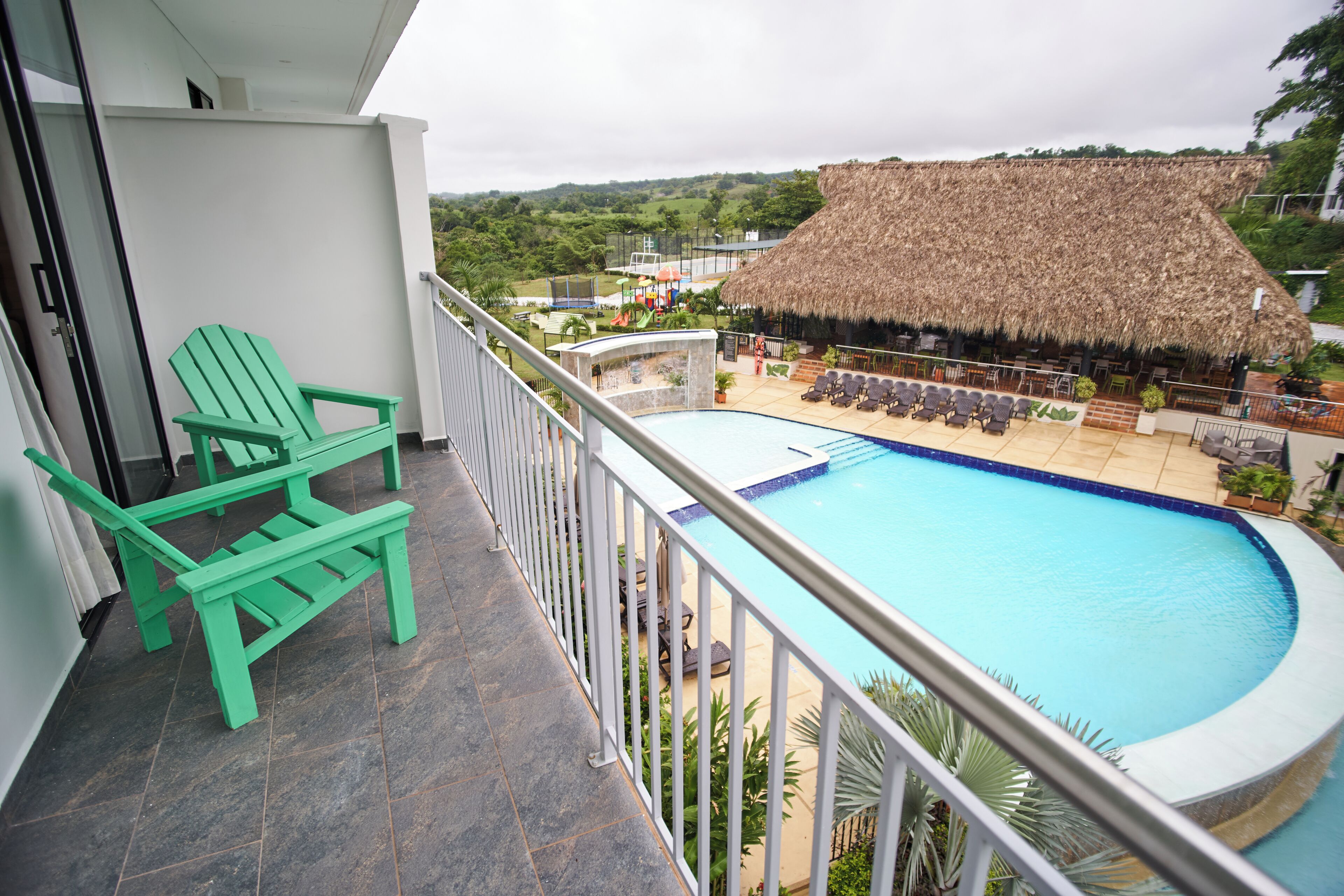 Un balcon avec une piscine, des chaises vertes et une structure surmontée d’un toit de chaume.