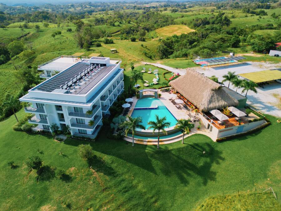 A resort with a swimming pool, a building with solar panels, and a thatched-roof structure.
