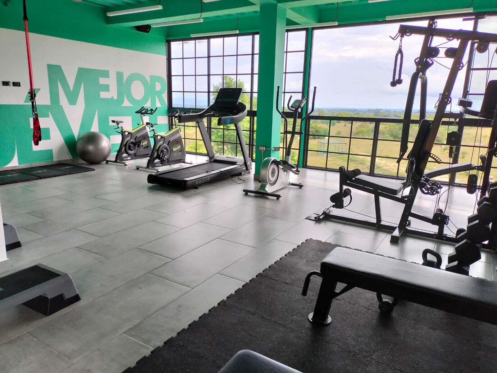 Un gimnasio con cintas de correr, bicicletas estáticas y equipo de pesas, amplias ventanas con vistas al exterior.