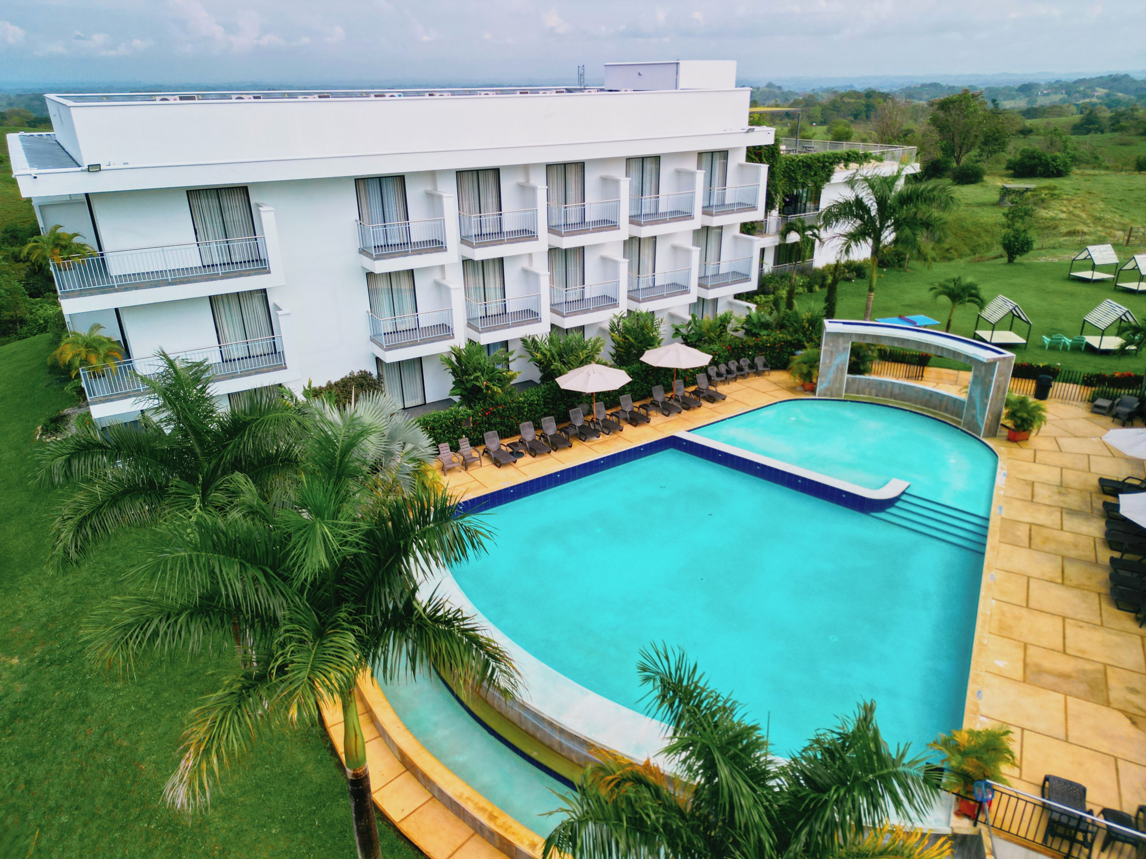 A modern hotel with a swimming pool, multiple balconies, and lush greenery.
