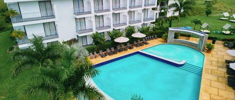 A modern hotel with a swimming pool, multiple balconies, and lush greenery.