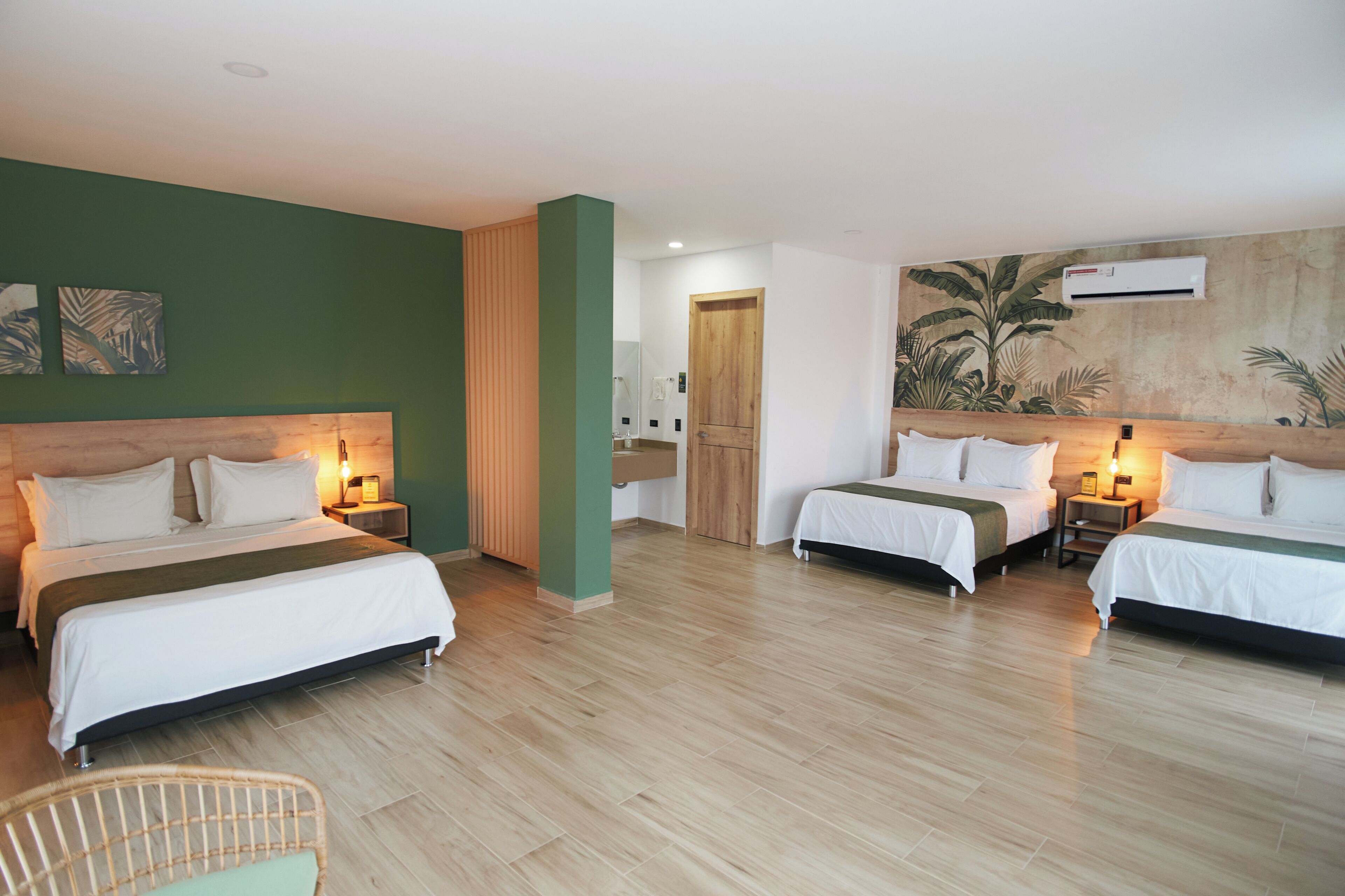Une chambre d’hôtel avec deux lits, un plancher en bois, un mur d’accent de couleur verte et un appareil de climatisation.