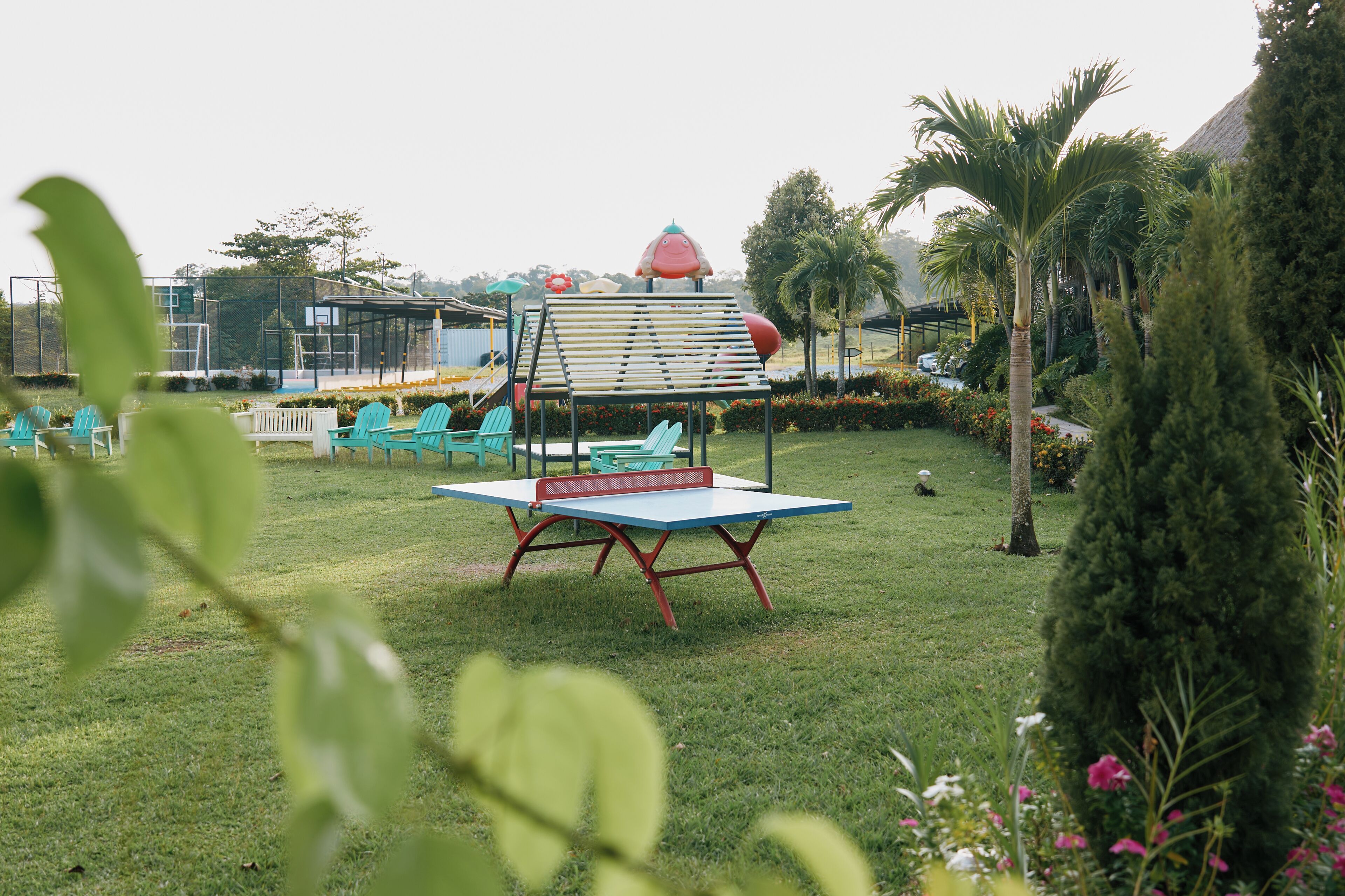 A grassy area with a ping pong table, several green chairs, and a small structure with a red roof.