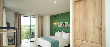 Un dormitorio con cama, escritorio, silla, balcón con vistas y una puerta de madera.